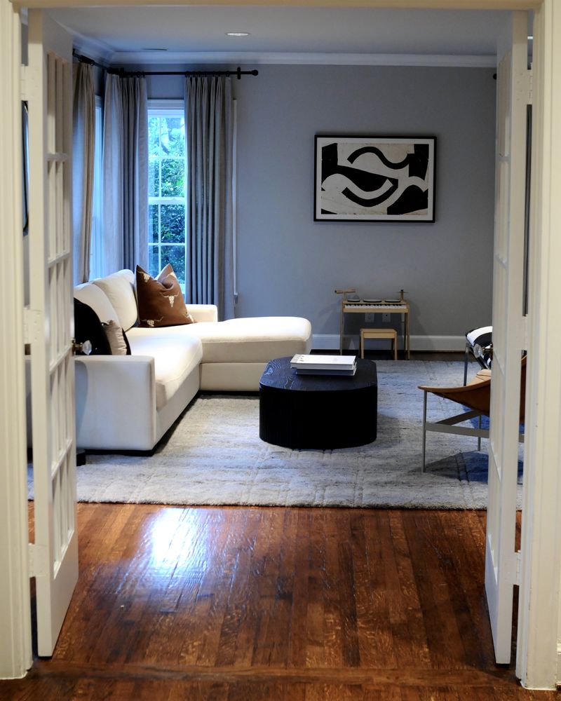 The living room through open French doors: a cream sectional, a round black coffee table and abstract art