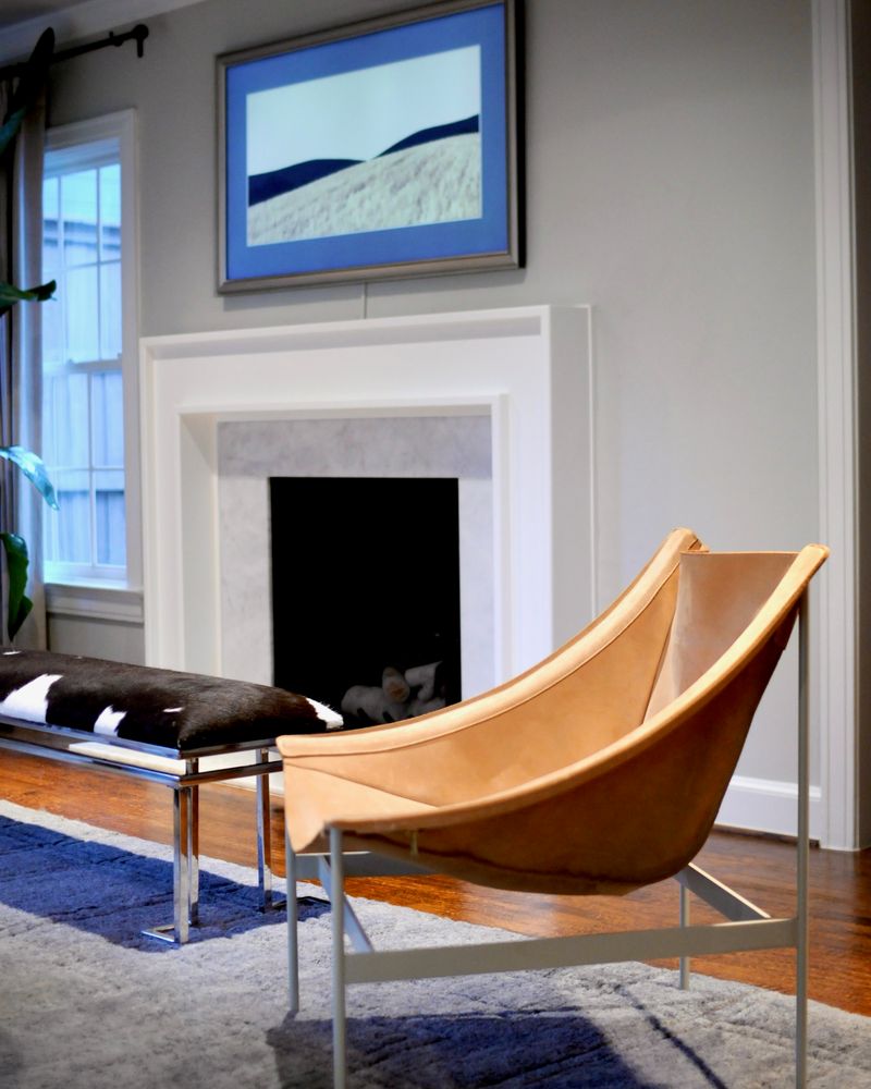 A tan leather sling chair in front of the fireplace